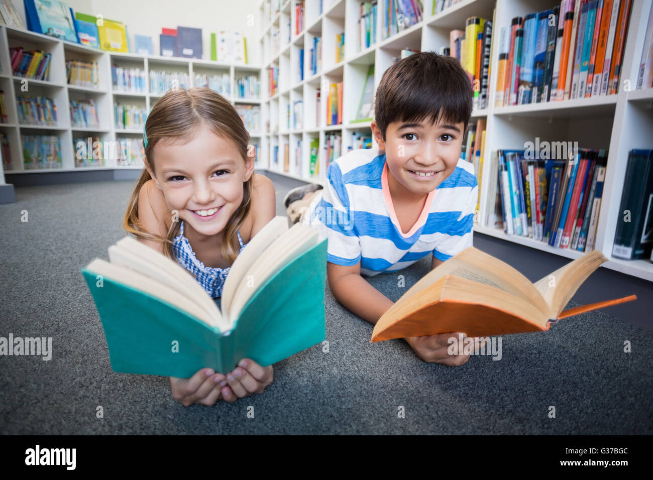 Happy school kids lying on floor and reading a book in library Stock ...