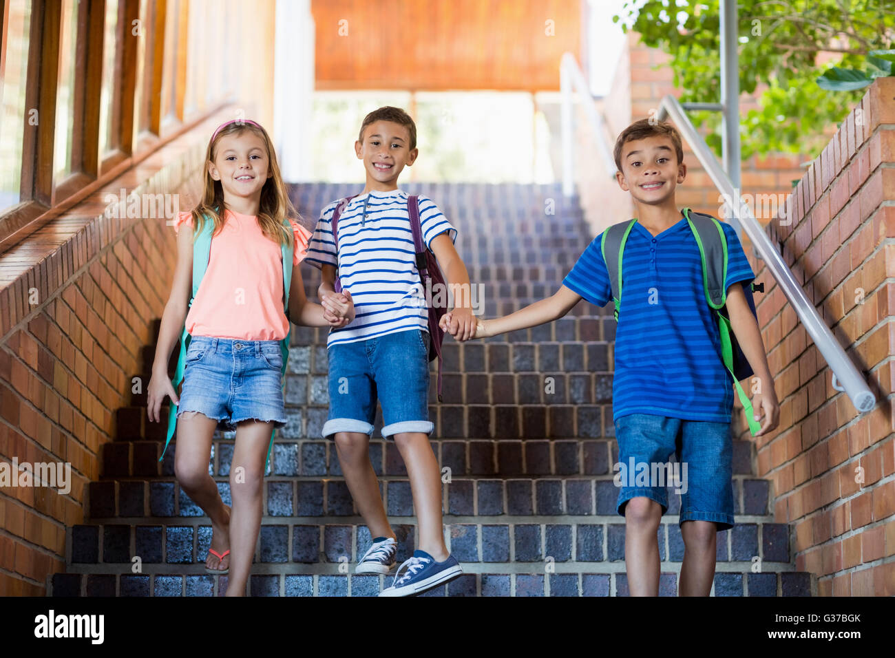 Happy school kids holding hands and walking on staircase Stock Photo