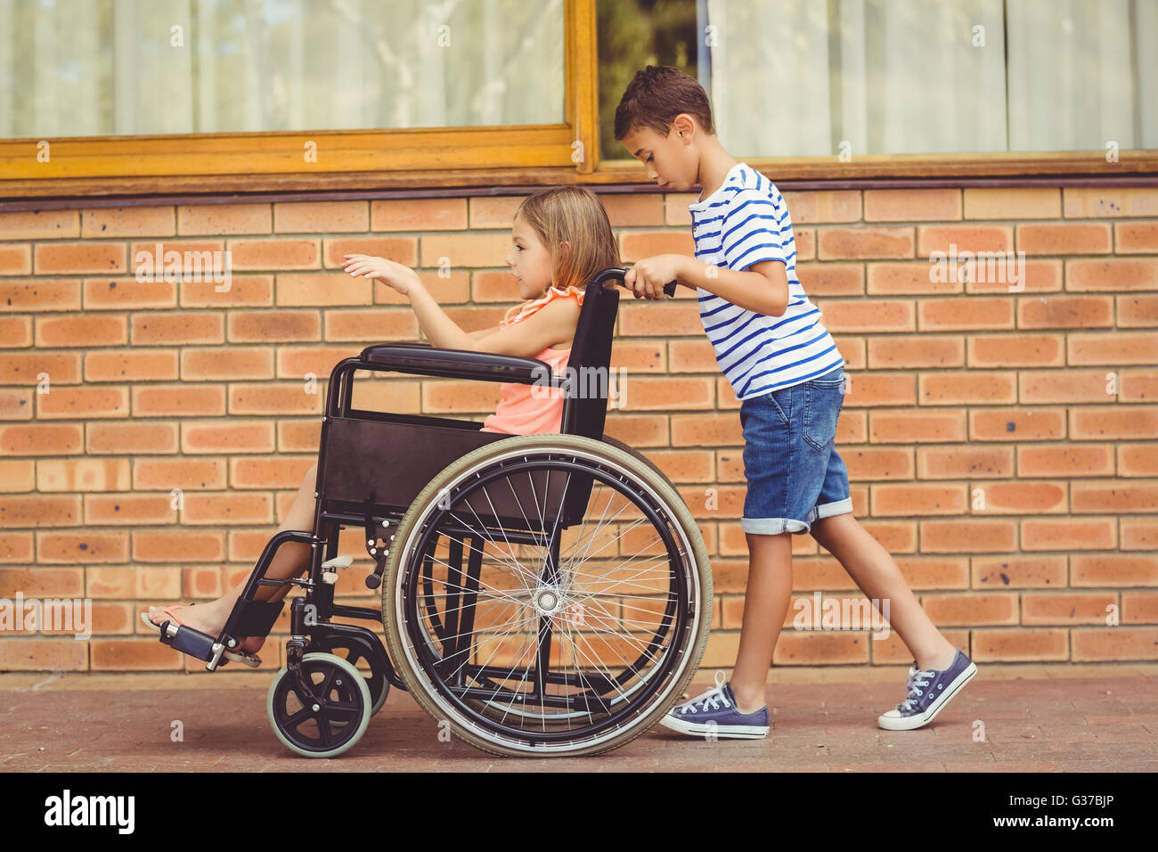 Schoolboy pushing a girl on wheelchair Stock Photo