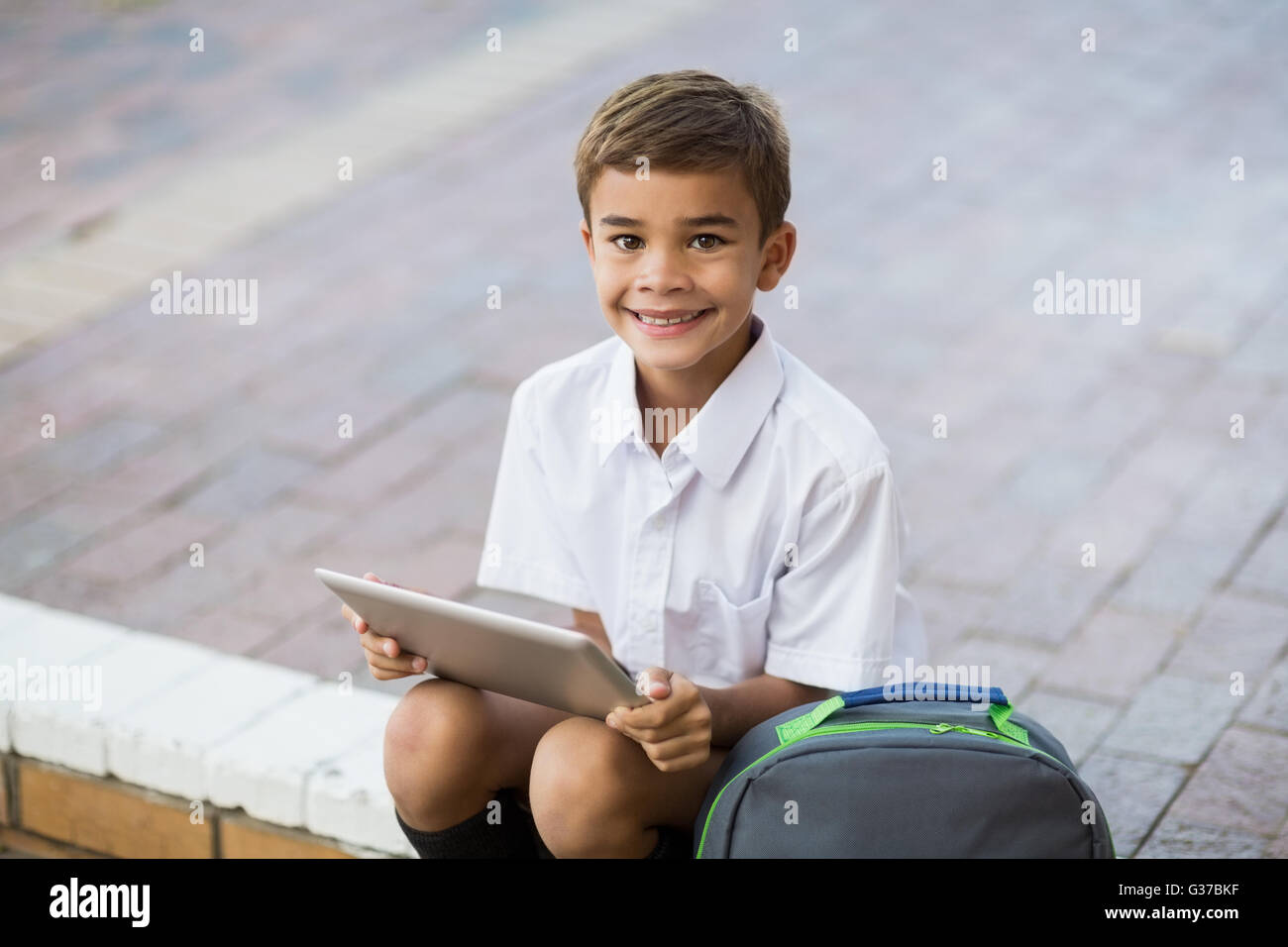 Happy schoolboy sitting in campus and using digital tablet Stock Photo ...