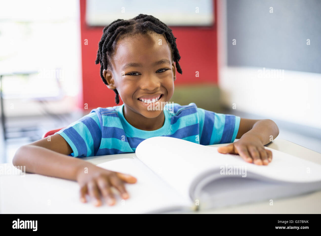 Portrait of smiling schoolboy reading book in classroom Stock Photo - Alamy