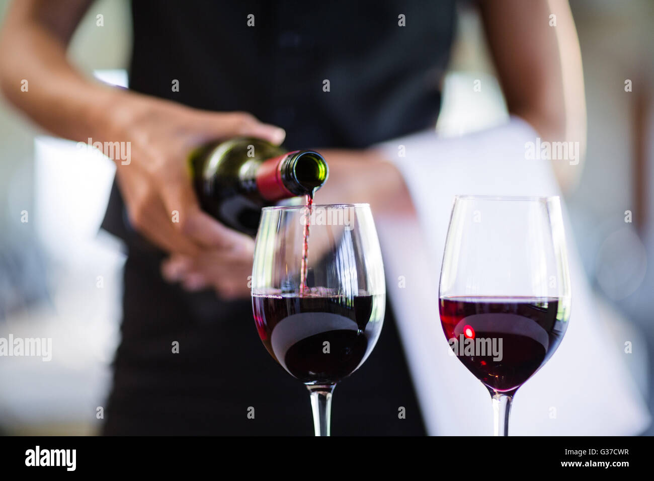 Mid section of waitress pouring red wine in a glass Stock Photo