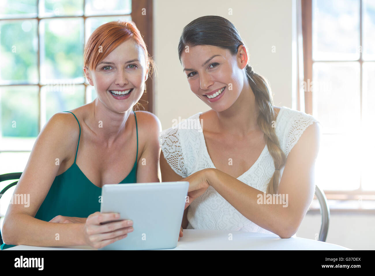 Two smiling women sitting in restaurant with a digital tablet Stock Photo