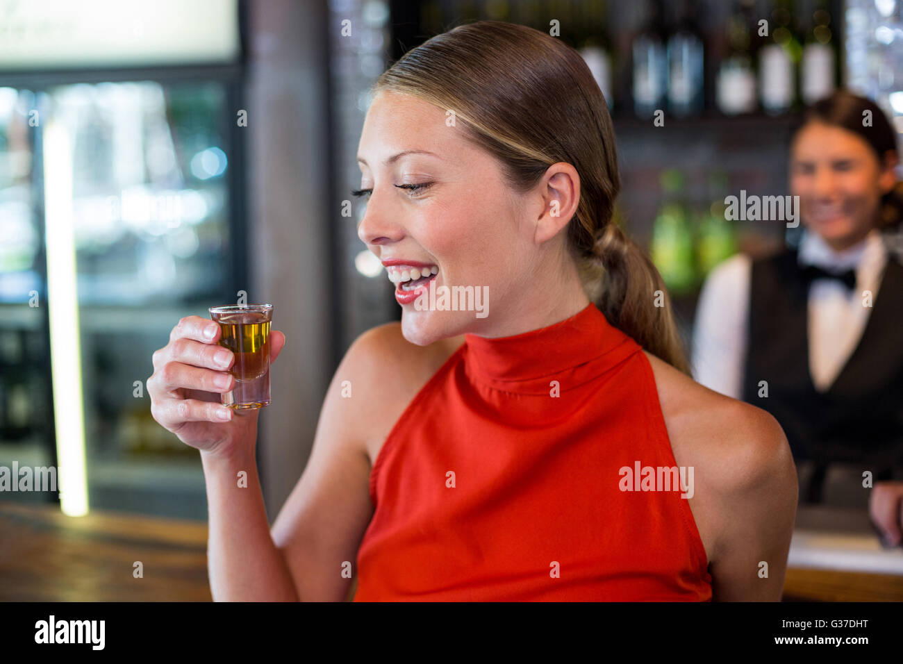 Happy woman holding a tequila shot in front of bar counter Stock Photo