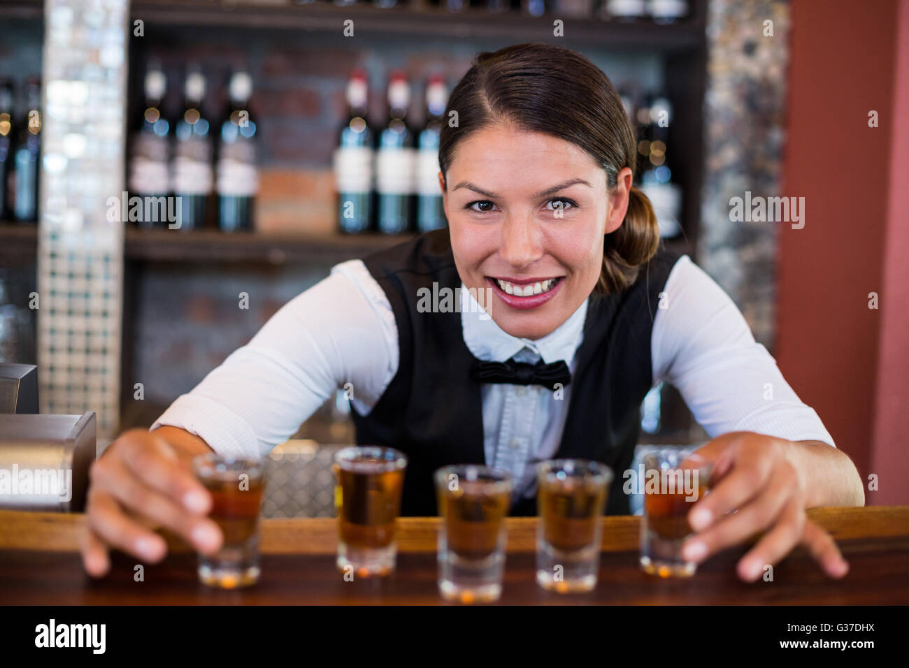 Portrait of bartender placing shot glasses on bar counter Stock Photo