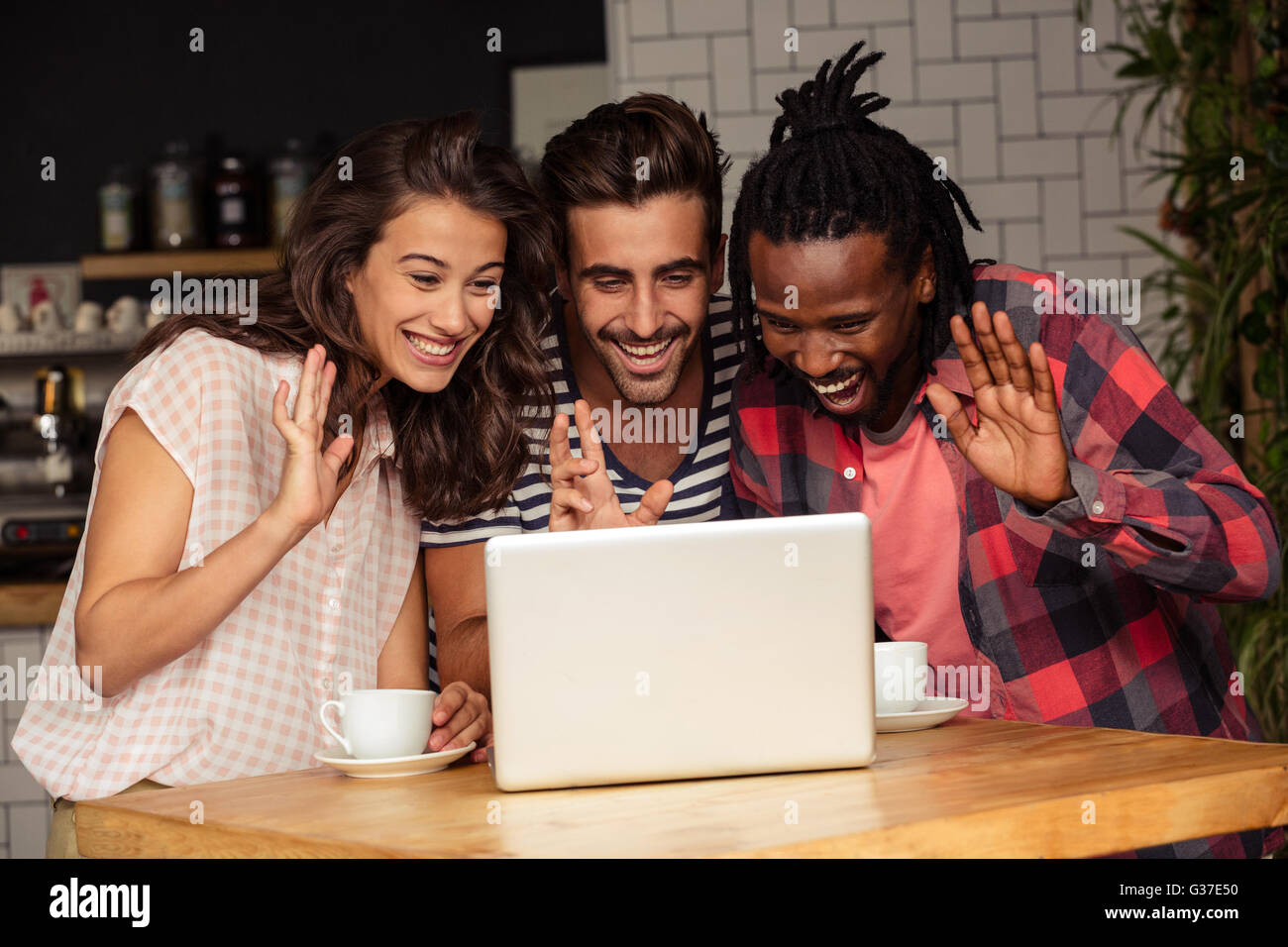 Friends greeting someone through the screen of a laptop Stock Photo