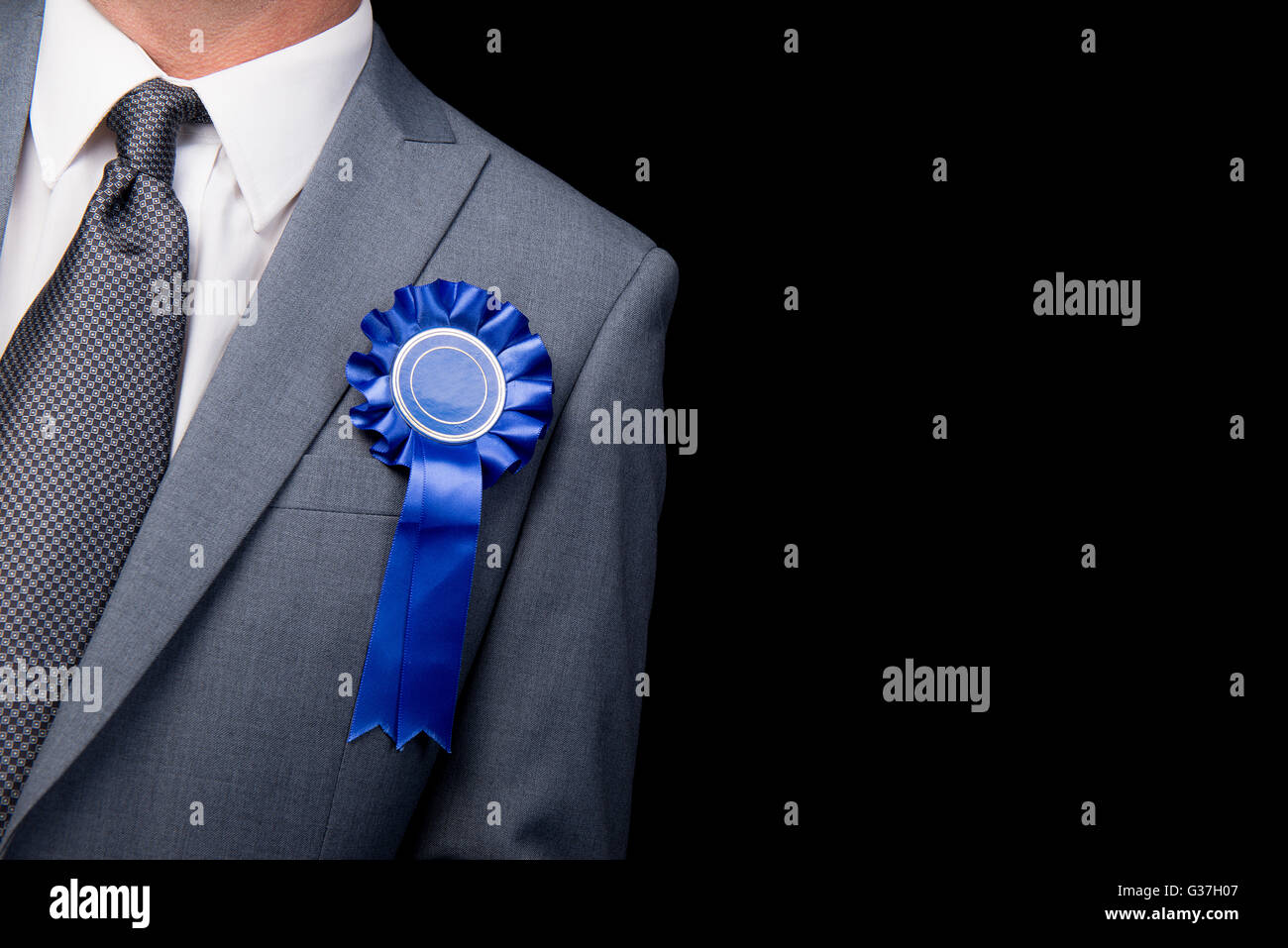 Head and shoulders view, of election candidate wearing a blue rosette, against a black background. Stock Photo