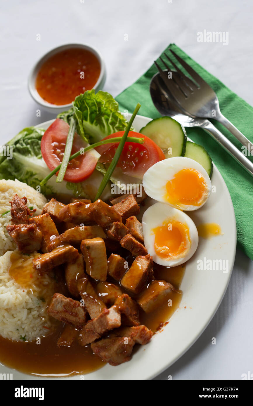 A traditional Thai dish of BBQ Pork with Rice (khao moo daeng) served with a side salad and soft boiled egg. Stock Photo