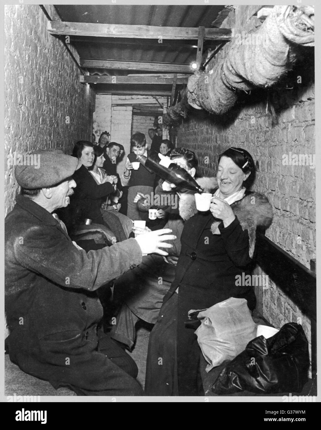 Sheltering underground during The Blitz in Islington, London;  a woman pours drinks for those around her      Date: November 1940 Stock Photo