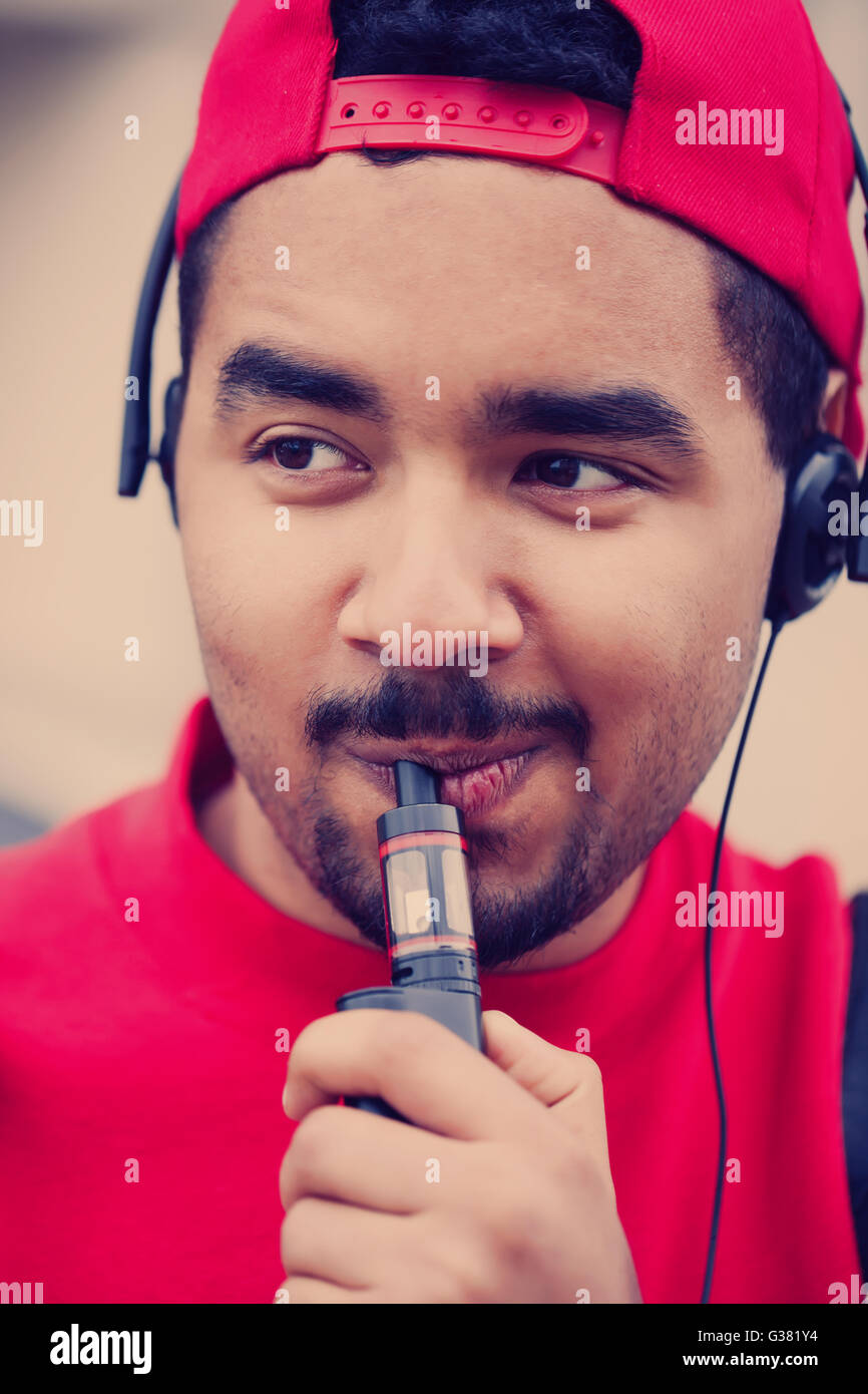 Portrait of black boy using modern e-cig vaporizer device for smoking glycerine liquid tobacco with flavor. Popular gadget among young people and who want to improve health and quit smoking Stock Photo