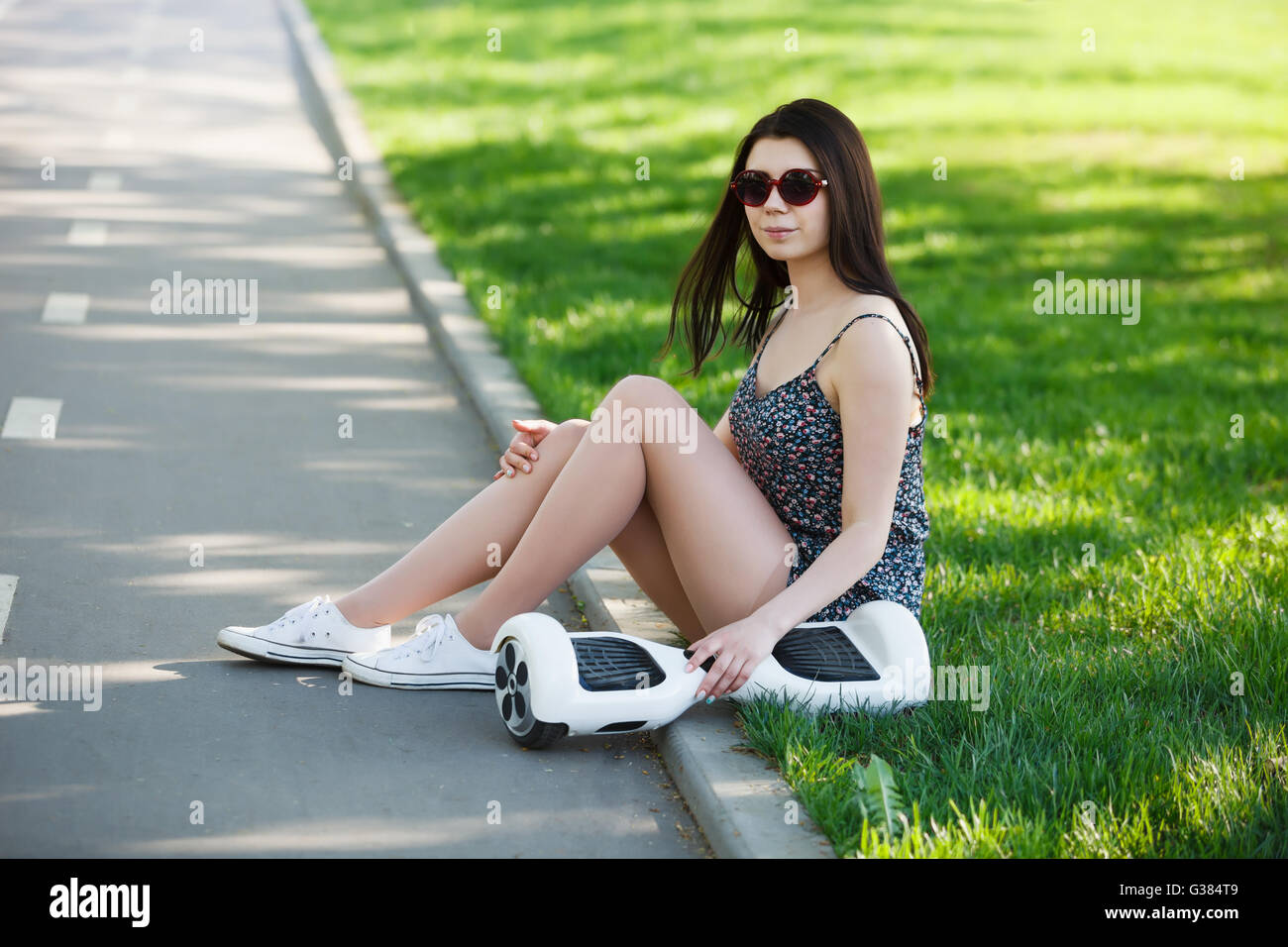 Young brunette girl riding electric mini hover board scooter in green park. Good summer weather, ecological eurban transportation technology and pretty model Stock Photo
