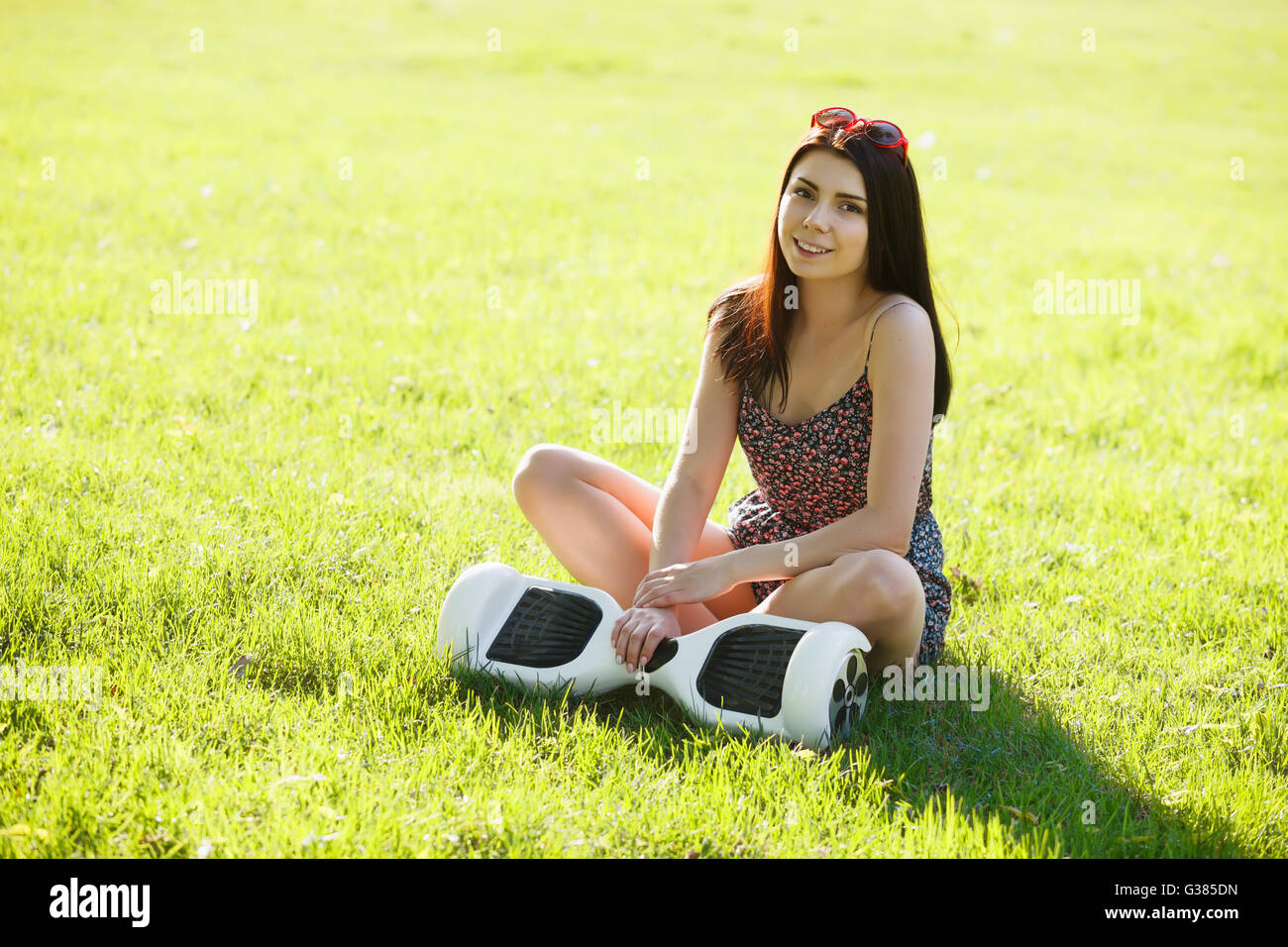 Young brunette woman with electrical mini hover board scooter in green park. Good summer weather, trendy transportation technology and cute model. Stock Photo