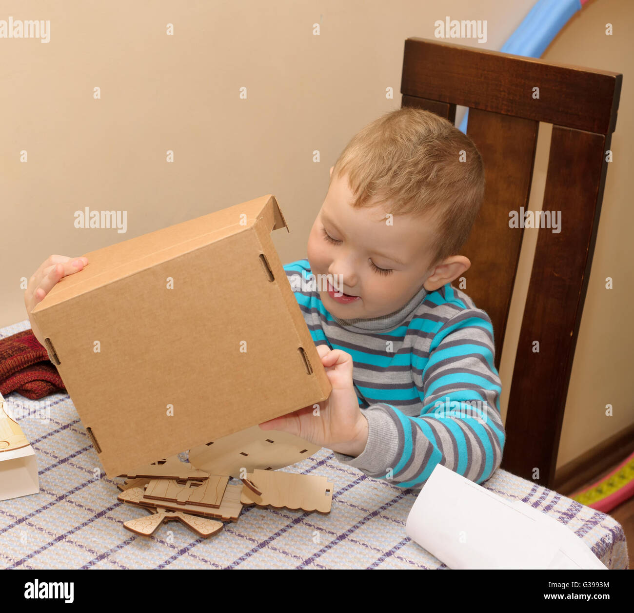 boy sitting at a table with a cardboard box in which lies a wooden constructor Stock Photo