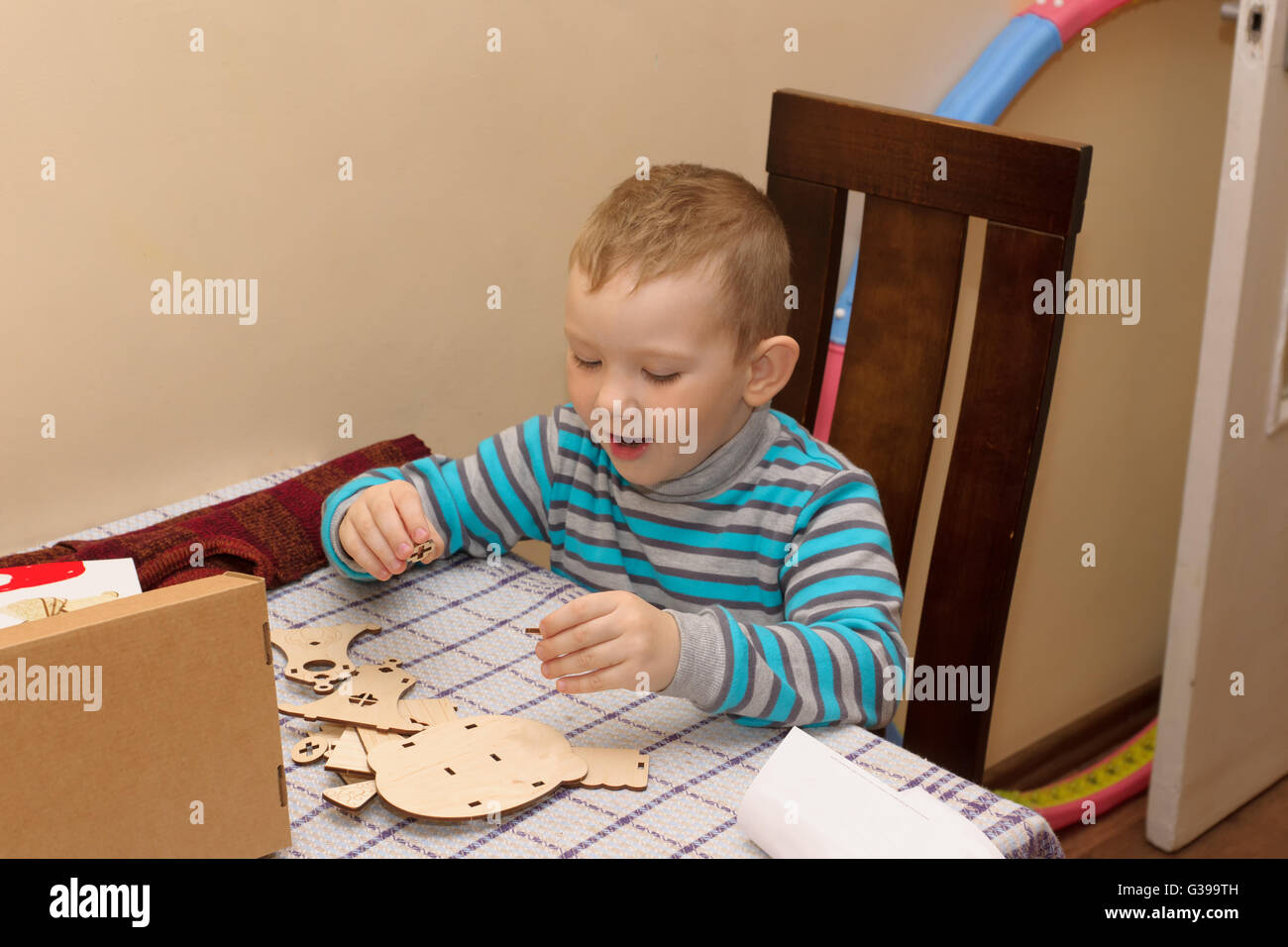 boy sitting at a table with a cardboard box in which lies a wooden constructor Stock Photo