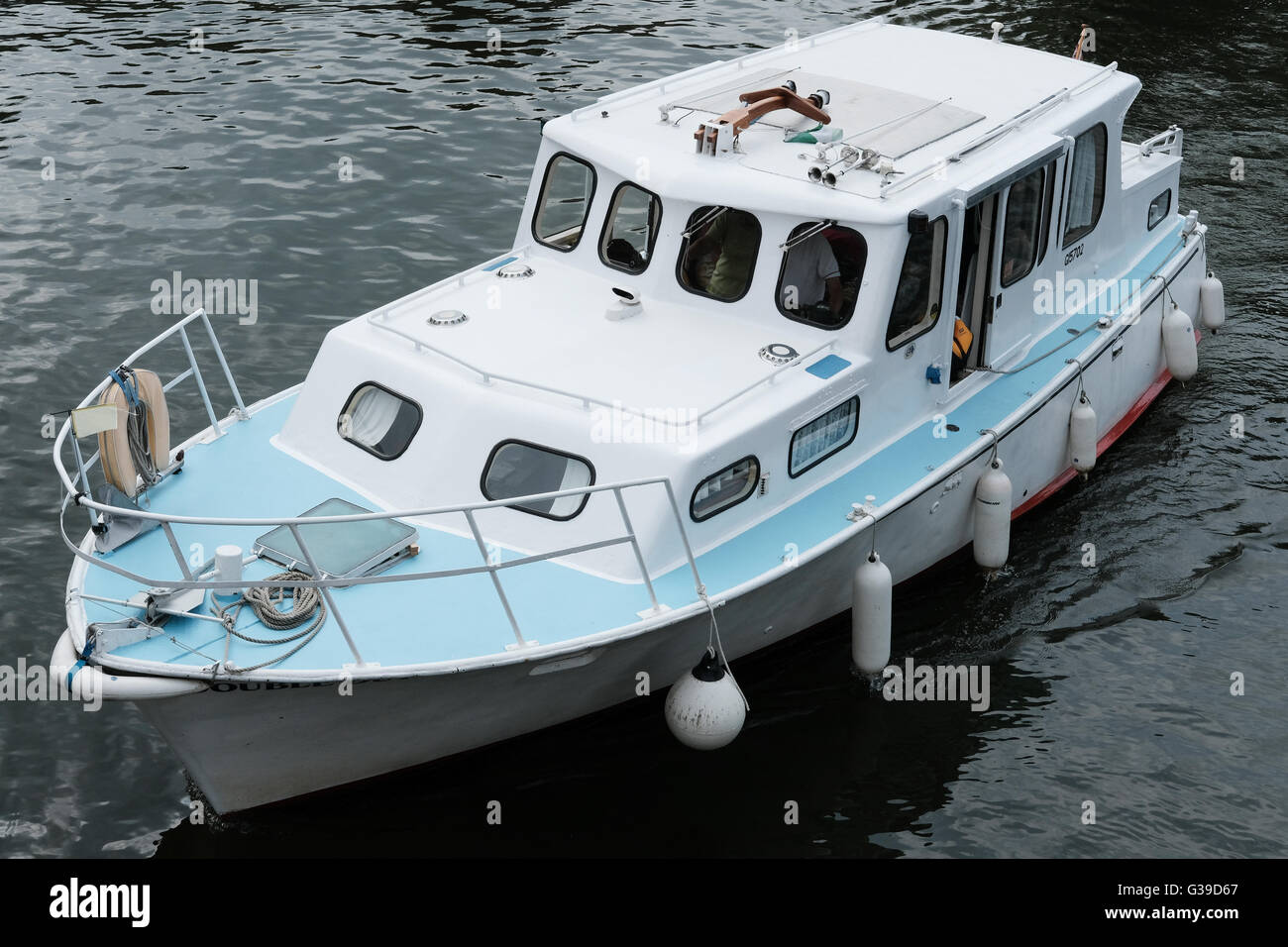 Small cabin cruiser boat seen sailing on a river way in a small market town  with the crew just visible on the bridge Stock Photo - Alamy
