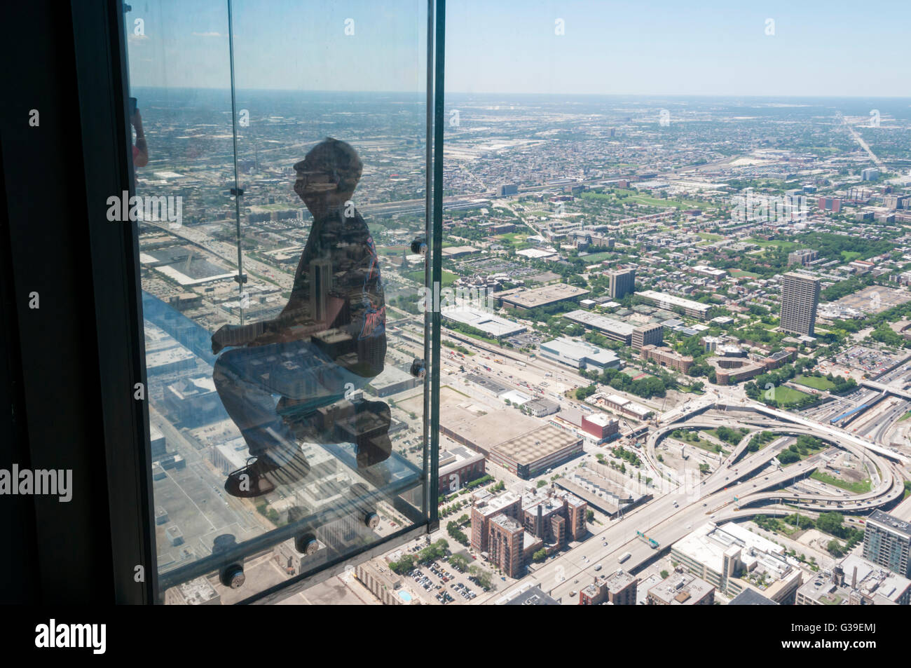 A man has his photograph taken on the glass balcony to the observation deck of the Willis Tower, with an aerial view of Chicago. Stock Photo
