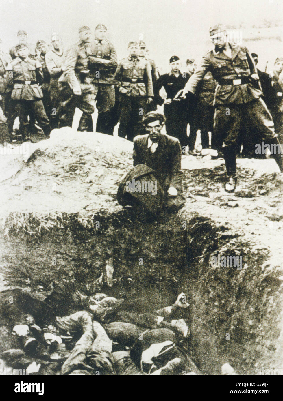 Mass murder in Poland.  A  soldier holds a gun to  civilian's head.  After he has  been shot he will topple into  a mass grave where a number of  bodies are already in a heap.     Date: 1942 Stock Photo