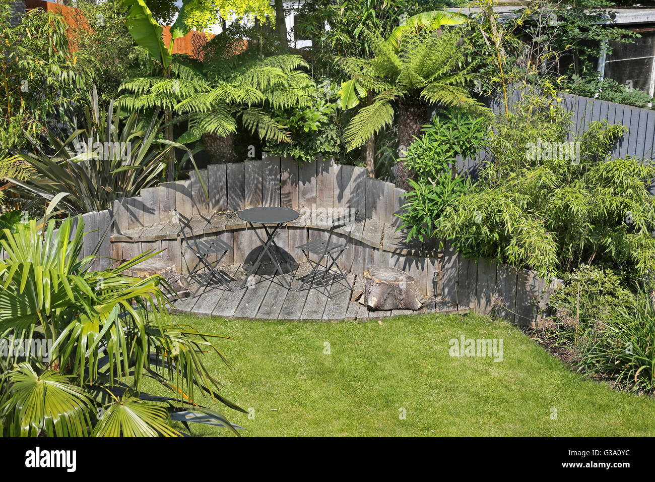 Decked seating area in a secluded London back garden featuring large, evergreen plants: tree ferns, bamboo, bananas and japonica Stock Photo