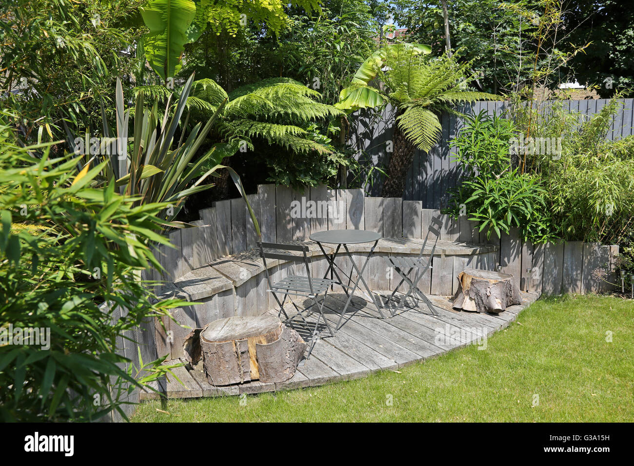 Decked seating area in a secluded London back garden featuring large, evergreen plants: tree ferns, bamboo, bananas and japonica Stock Photo