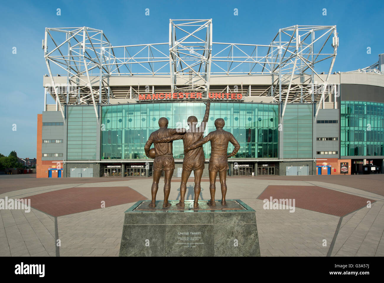 Old Trafford, the stadium of Manchester United Football Club, with the United Trinity statue on a sunny day (Editorial use only) Stock Photo