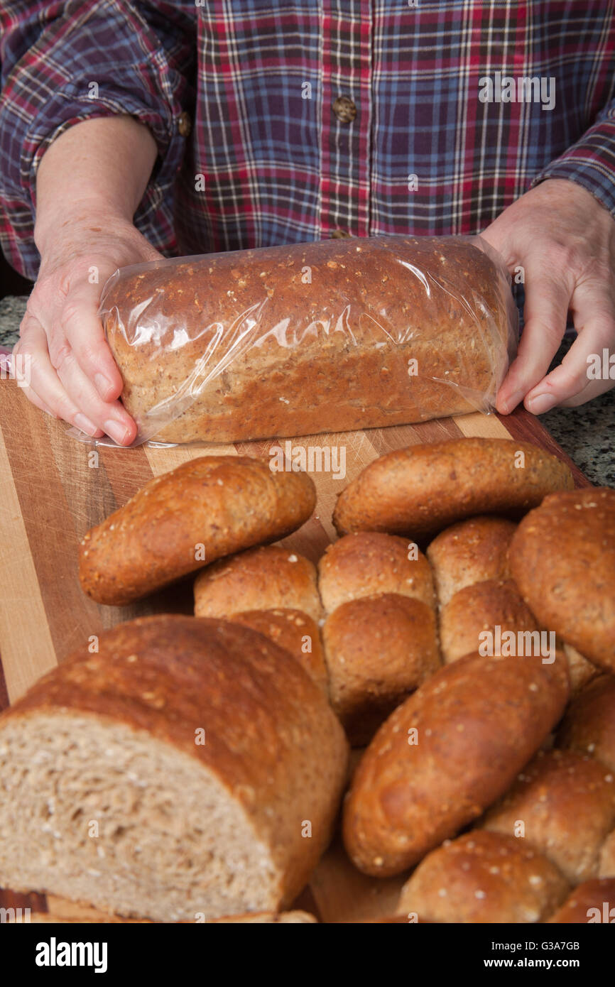 Woman placing a loaf of multigrain bread into a plastic bag to store it Stock Photo