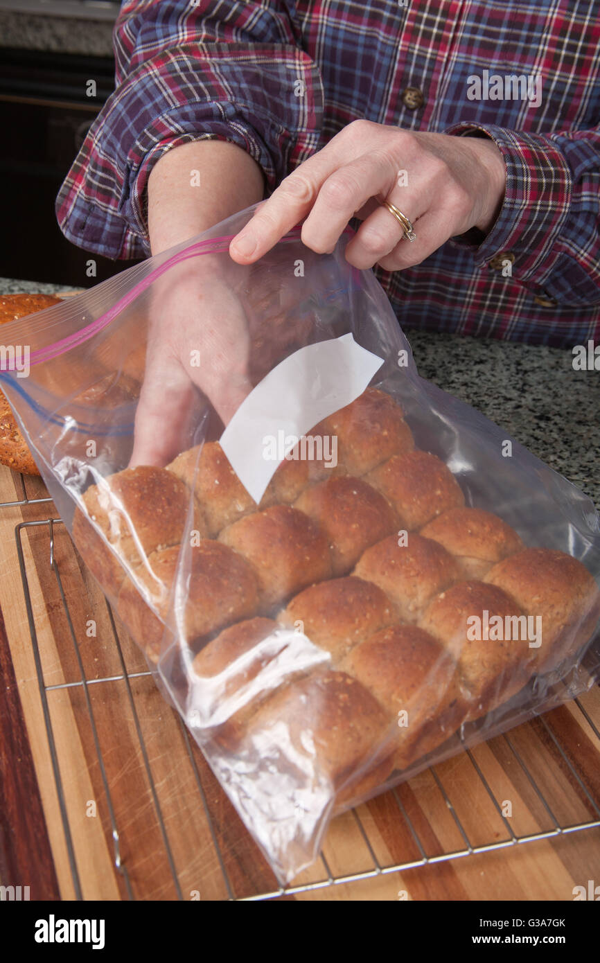 Woman placing multigrain bread rolls into a plastic bag to store them Stock Photo