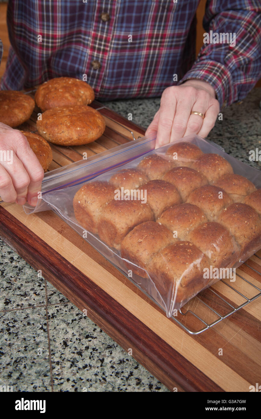 Woman placing multigrain bread rolls into a plastic bag to store them Stock Photo