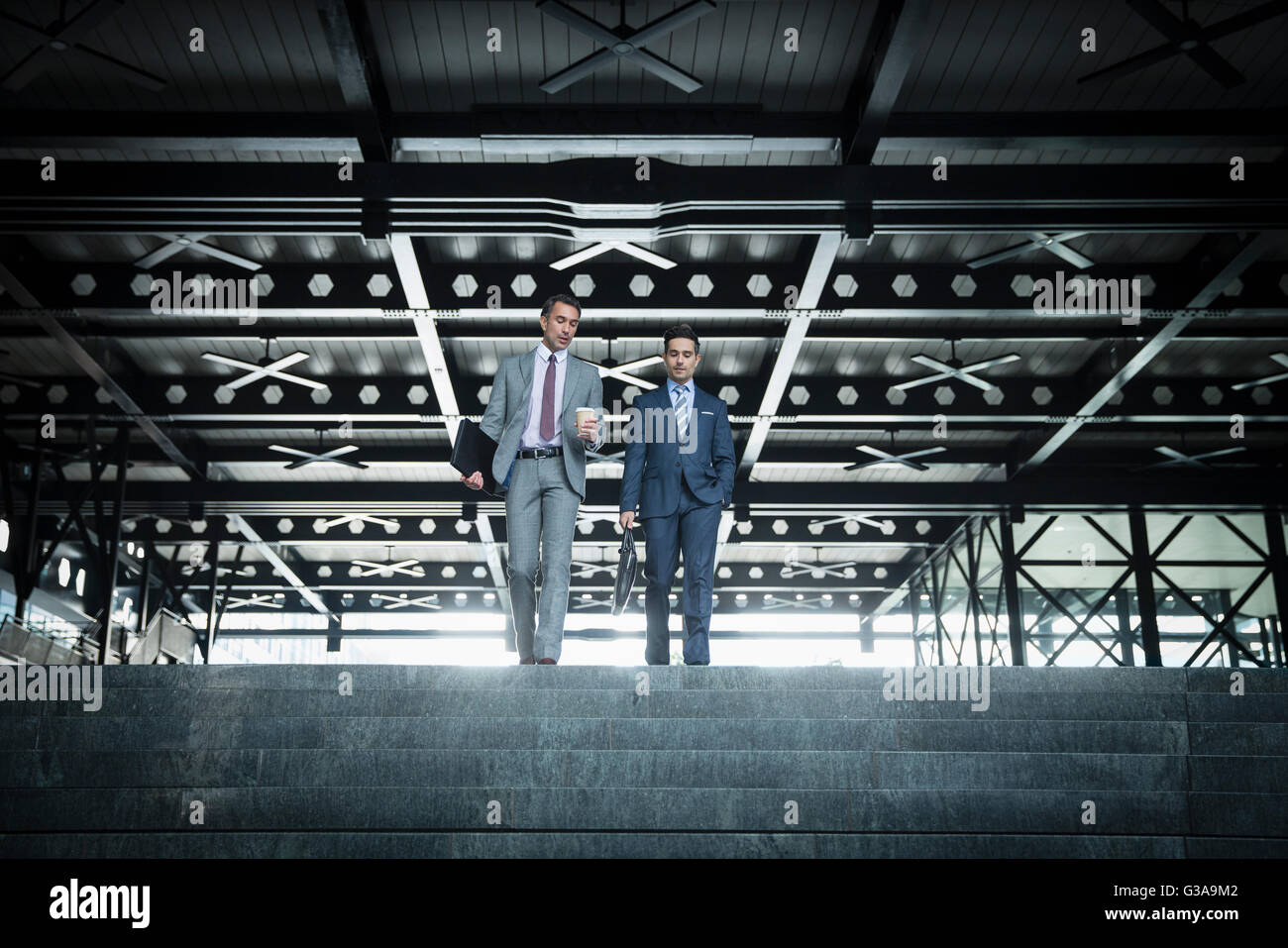 Corporate businessmen with coffee descending modern stairs Stock Photo