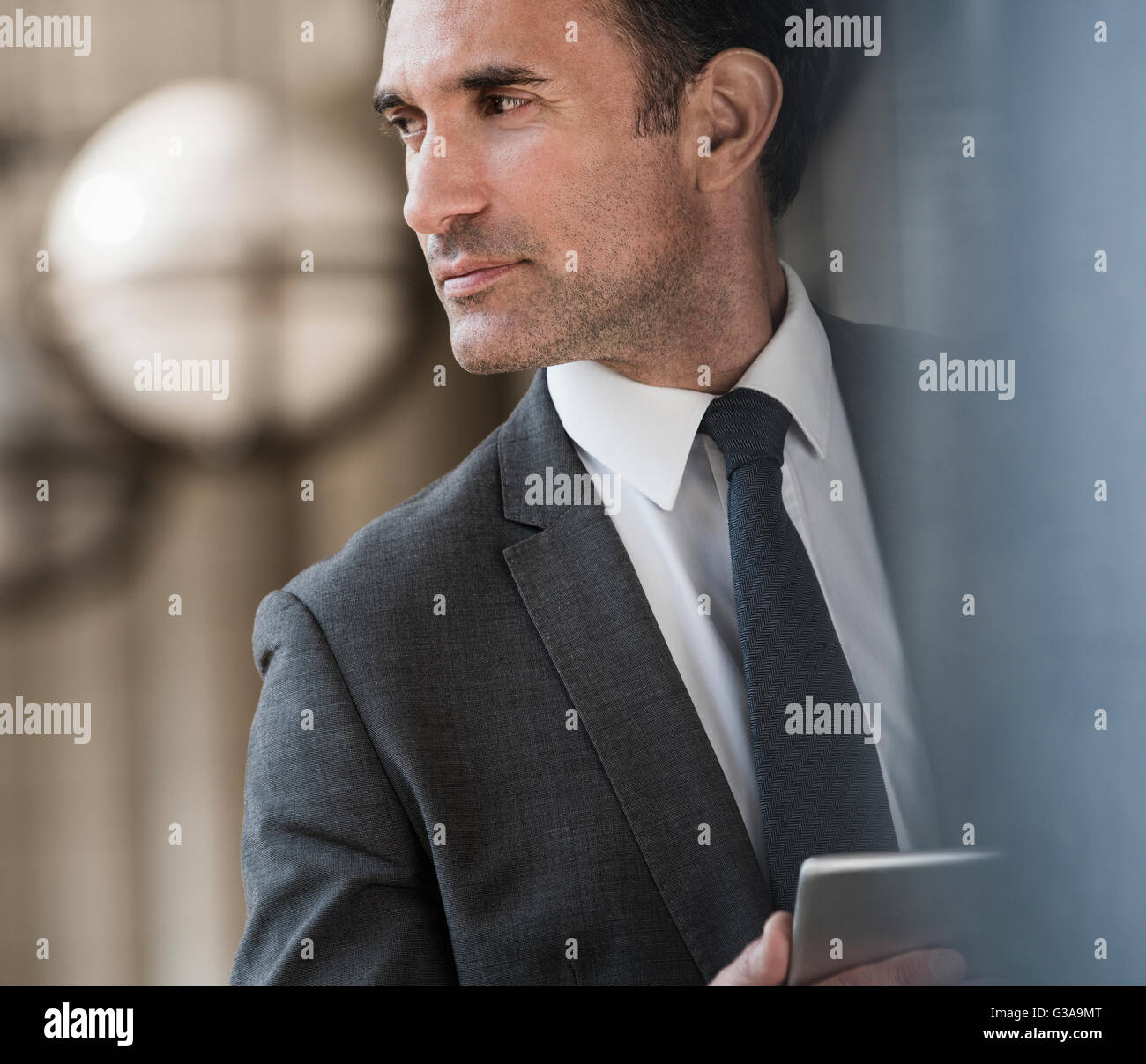 Pensive corporate businessman with digital tablet looking away Stock Photo