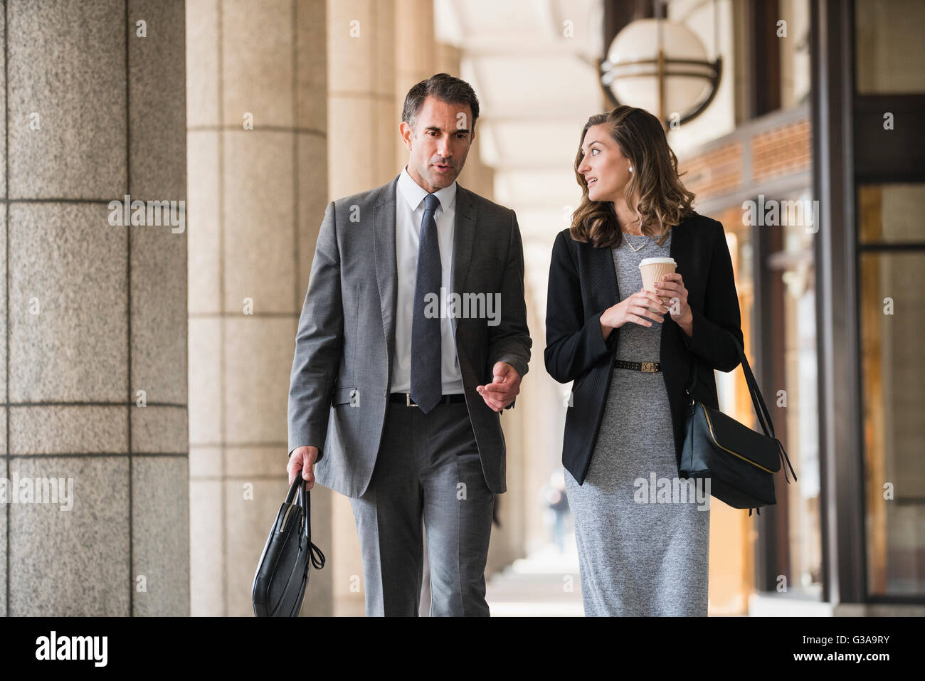 Corporate businessman and businesswoman with coffee walking and talking in cloister Stock Photo
