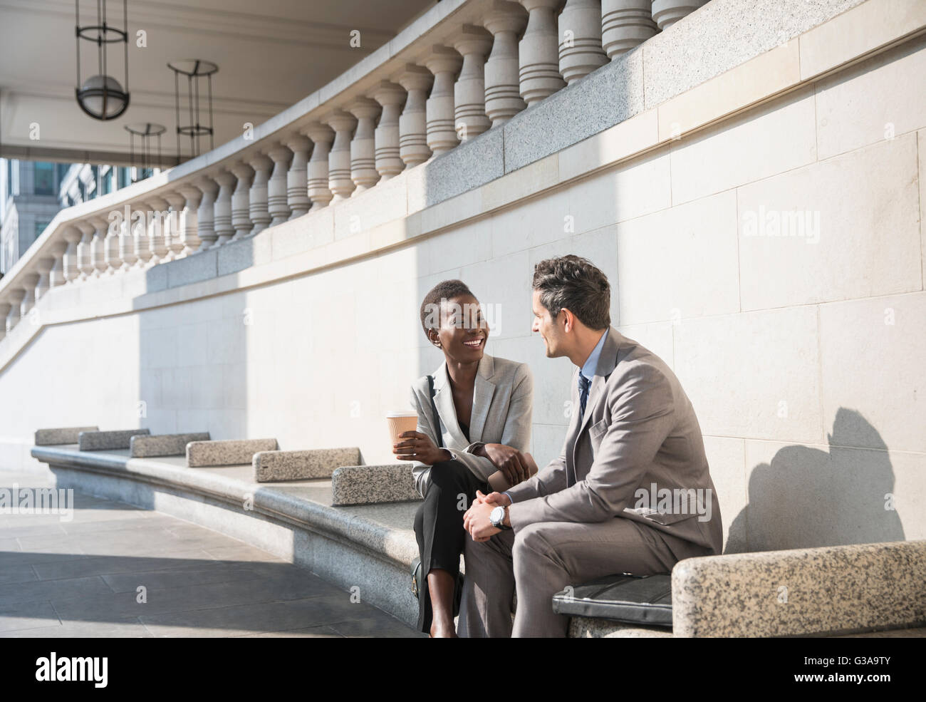 Corporate businessman and businesswoman enjoying coffee break on sunny stairs Stock Photo