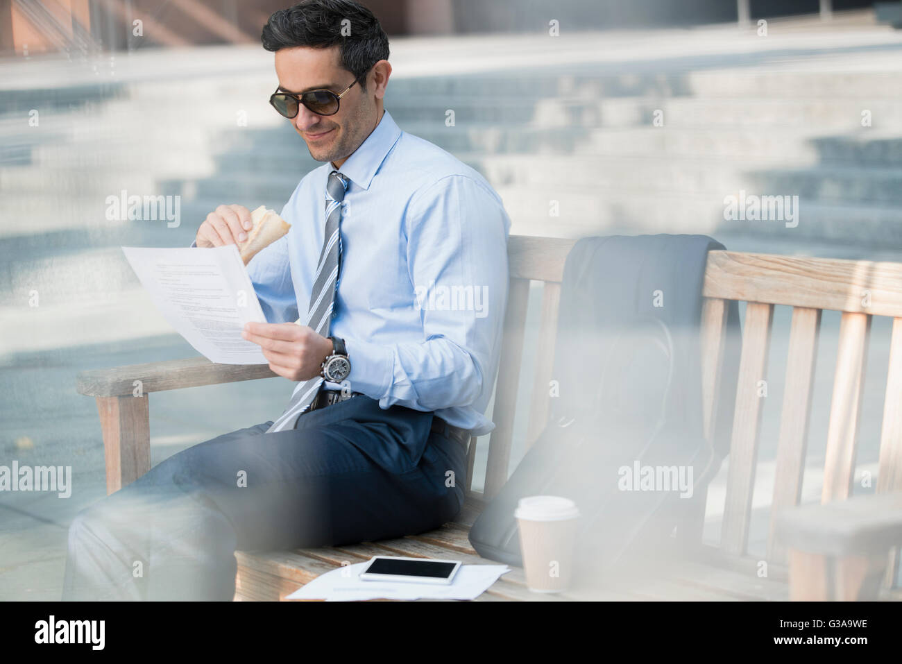 Corporate businessman eating lunch and working on bench Stock Photo