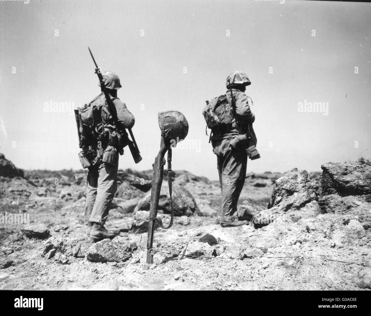 Two Marines in the First Battalion, 26th Marines move past the temporary grave of a Marine, marked by his rifle and helmet. Stock Photo