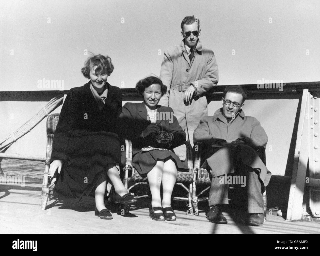 Slightly windswept passengers on deck aboard the ferry on the way to a Holiday in Norway. Sitting on wicker chairs close to the rail, wrapped up in raincoats and mittens!     Date: early 1950s Stock Photo
