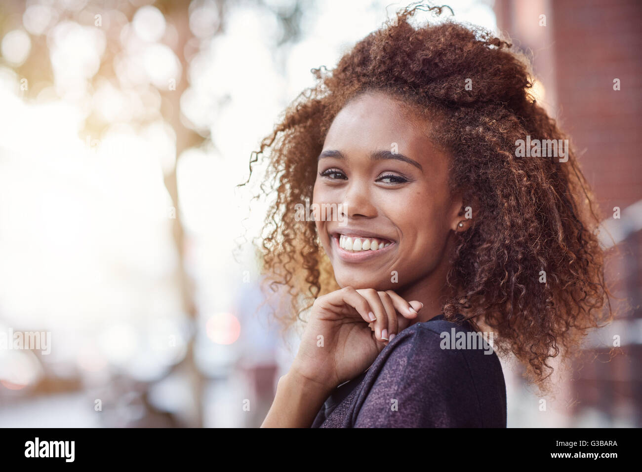 Portrait of a beautiful young woman with curly hair out in the city ...