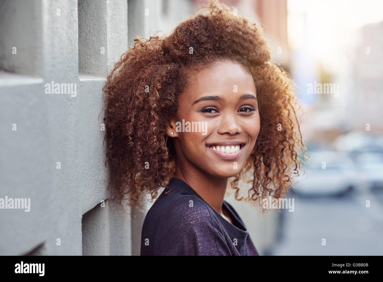 Portrait of a beautiful young woman with curly hair out in the city ...