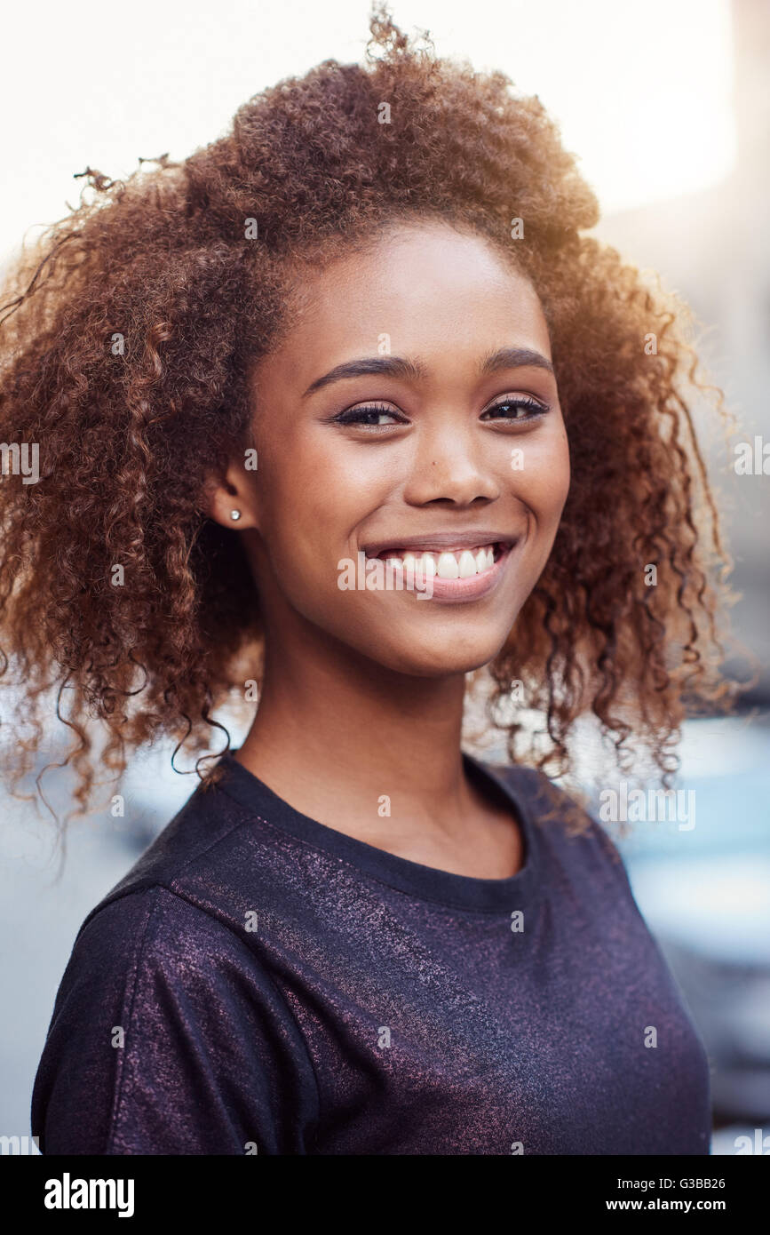 Portrait of a beautiful young woman with curly hair out in the city ...