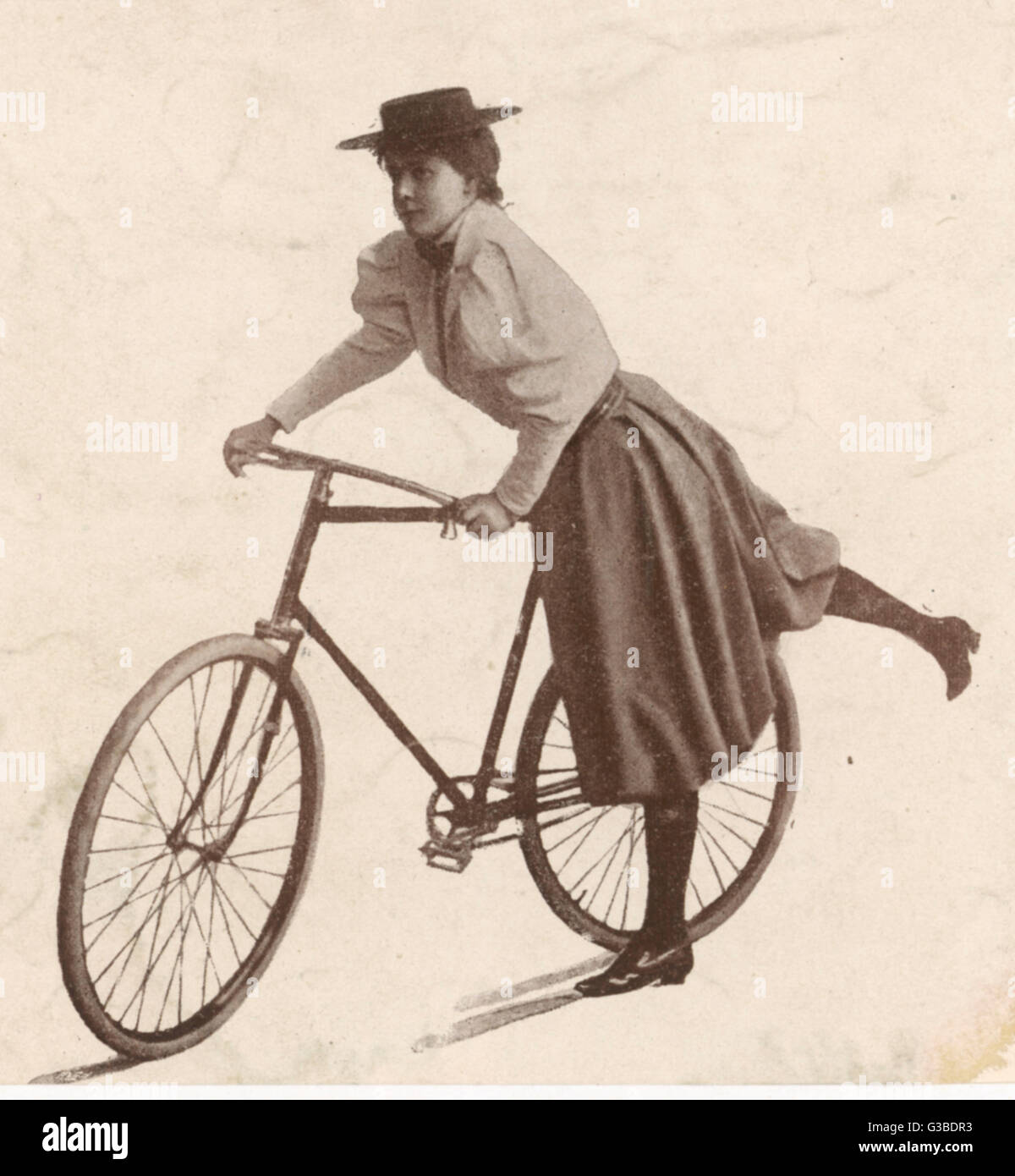 A sporty young Frenchwoman  mounts her bicycle - a man's  model, with crossbar : she is  wearing a practical and  picturesque divided skirt,      Date: circa 1896 Stock Photo
