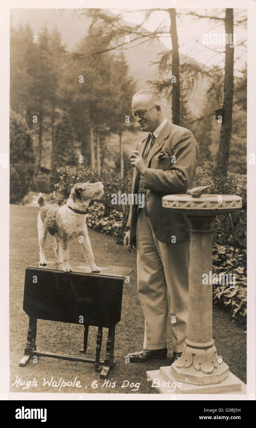 The popular novelist Hugh Walpole and his wire-haired fox terrier Bingo, in the  garden of their home at  Keswick, Cumbria.      Date: 1930s Stock Photo