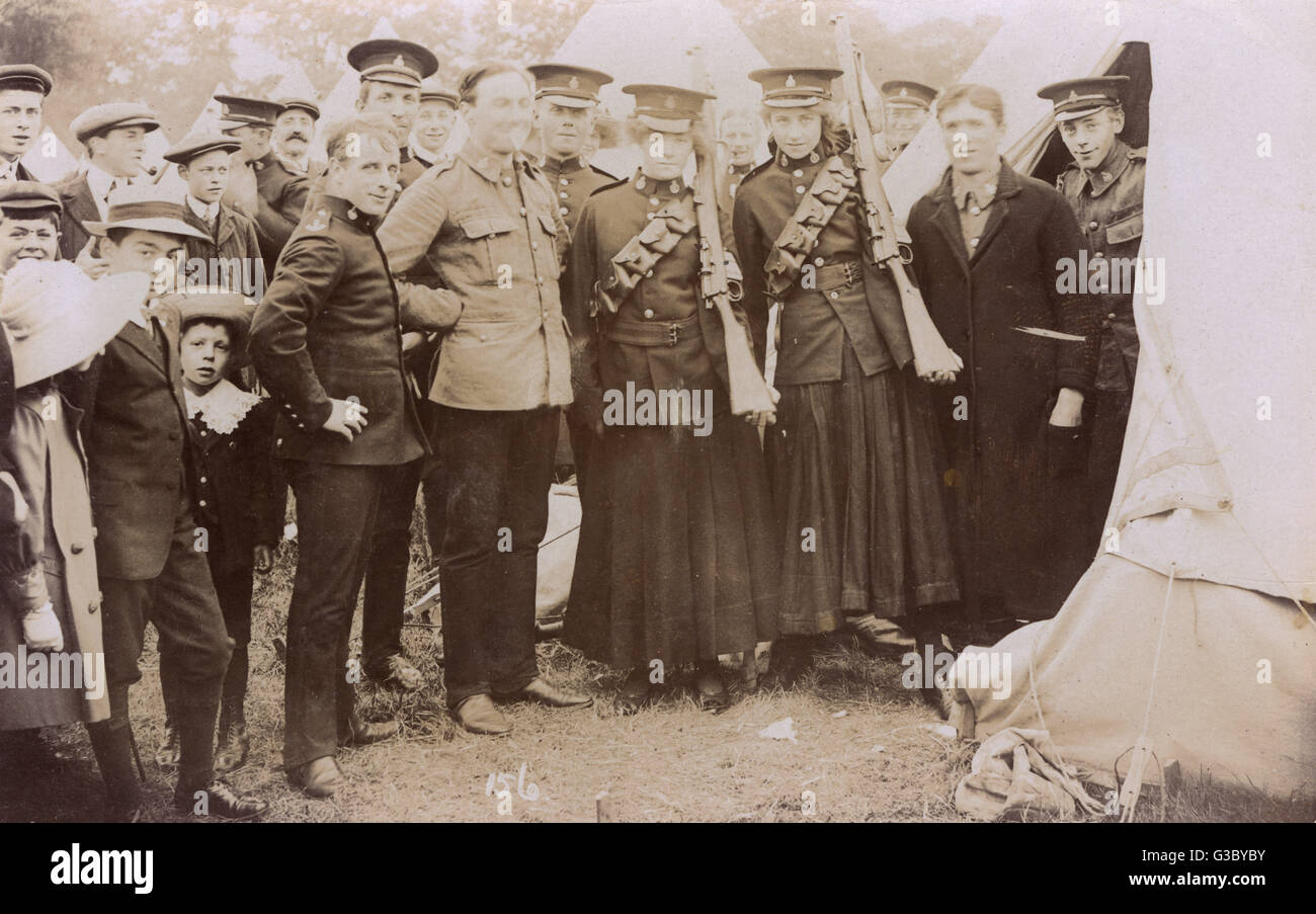 Group photo, British soldiers (including two young women in uniform, with rifles) and civilians, at a camp.      Date: circa 1914 Stock Photo
