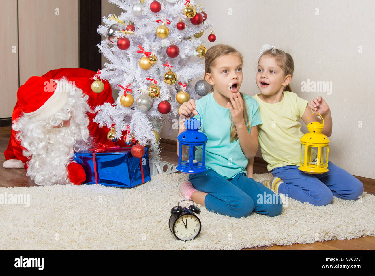 Two girls with flashlights dreaming of gifts on New Years night, and Santa Claus put presents under the Christmas tree Stock Photo