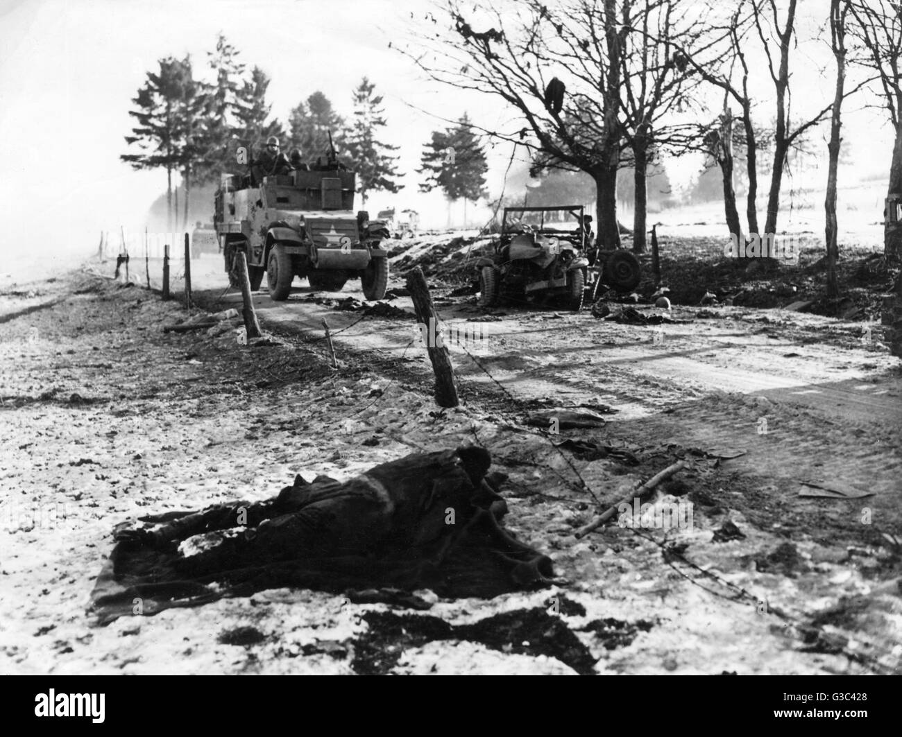 An American armoured vehicle passes the wreckage of a jeep on an Ardennes road during the Battle of the Bulge     Date: 1945 Stock Photo