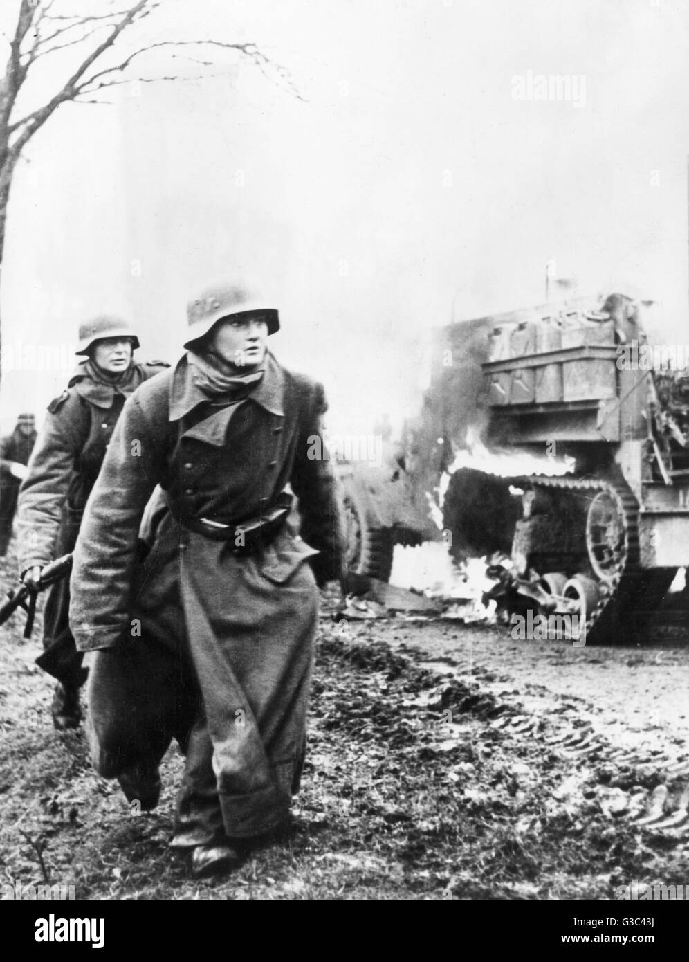 German soldiers advance past a burning American half-track vehicle during the counter-offensive in  the Ardennes, Belgium, which became known as the Battle of the Bulge.     Date: December 1944 Stock Photo