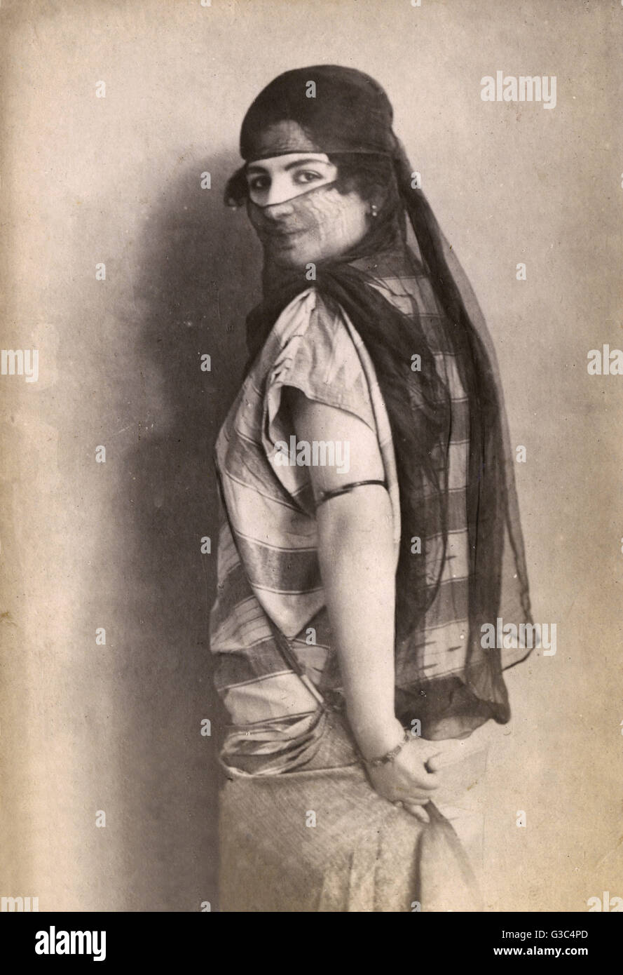 Veiled Turkish Woman turns with a coy gaze toward the photographer.     Date: 1920s Stock Photo