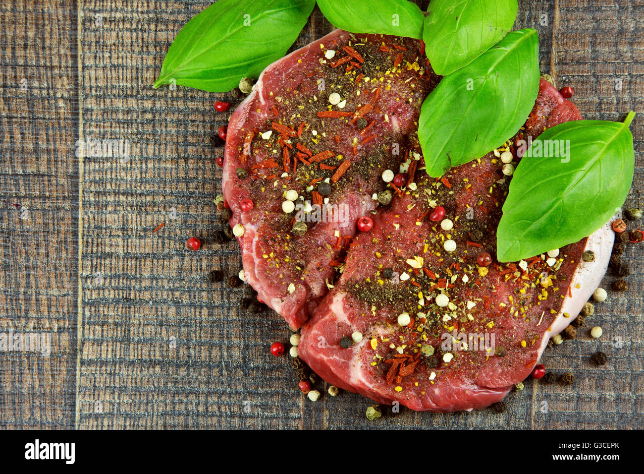 Two raw sirloin steaks sprinkled with spices and fresh basil leaves on