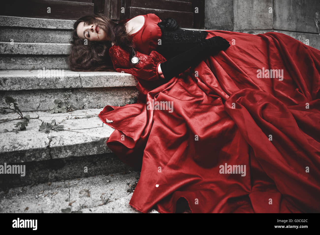Lying and bleeding woman in a red Victorian dress Stock Photo