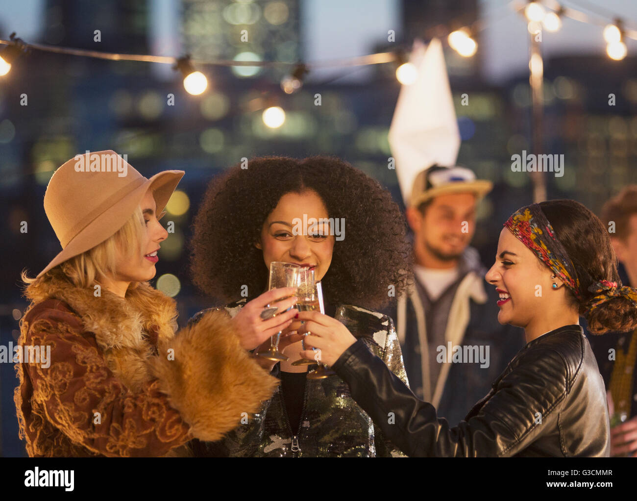 Young women toasting champagne glasses at nighttime rooftop party Stock Photo