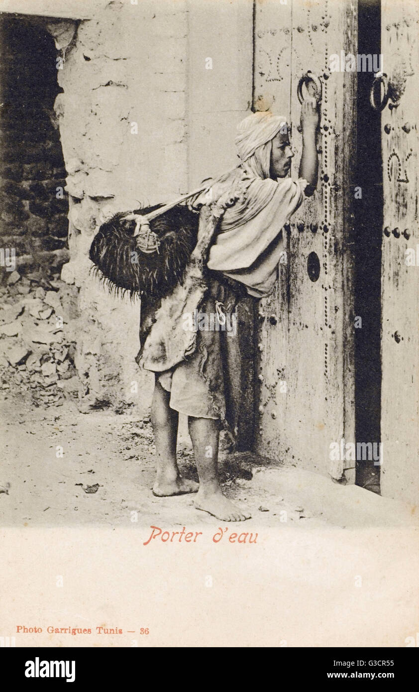 Tunisia, Water Carrier knocking at an impressive wooden door Stock Photo