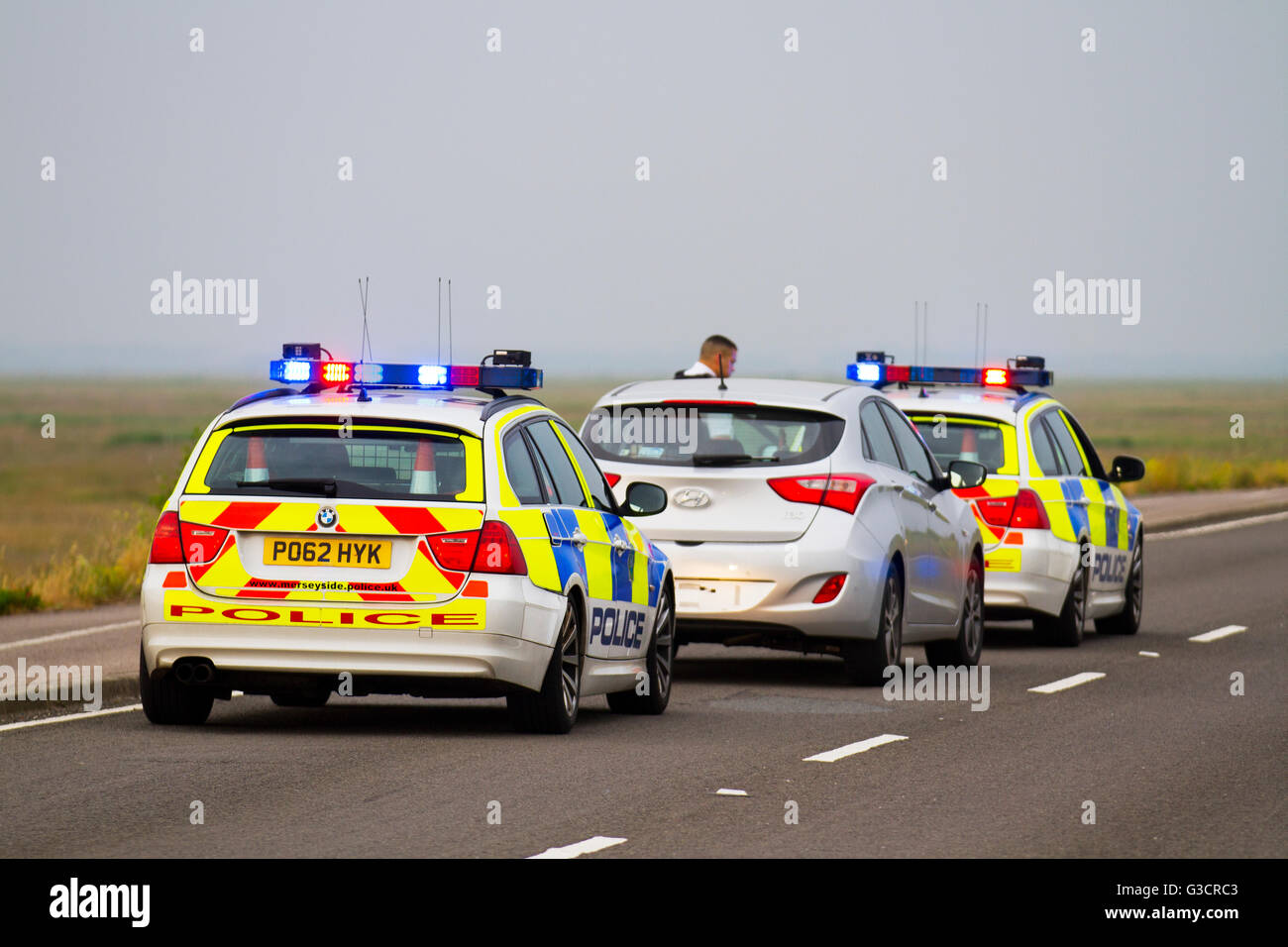 British Traffic policemen on Emergency 999 Response. British Police patrol cars attending vehicle traffic stop on Marine Drive, Southport promenade, Merseyside UK.  Two police vehicles were used in a pursuit tactic, as well as using red and blue lights to pull over the motorist speeding. Stock Photo