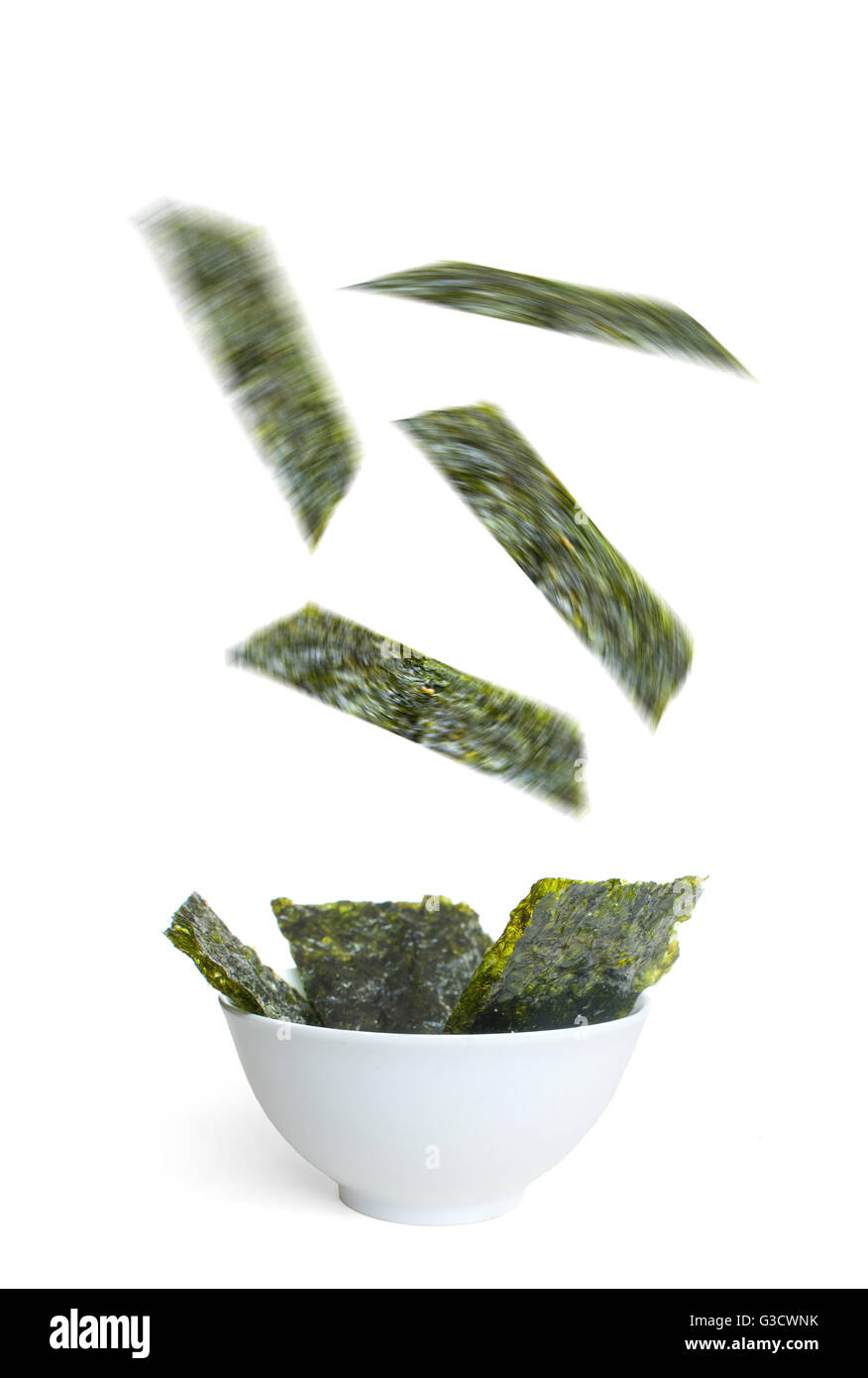 Seaweed slices falling into a bowl over a white background, a superfood that is high in vitamin c, iron and promotes healthy bac Stock Photo